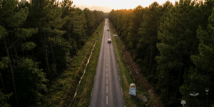 Vue aérienne d'une longue route départementale rectiligne traversant la forêt de pins des Landes au coucher du soleil, illustrant les spécificités d'infrastructure et les risques d'accidentologie locale.